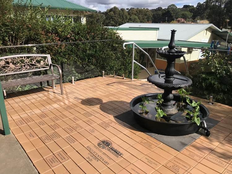 Our sesquicentenary garden, paved with student and staff names on pavers, a fountain in the centre, 2 garden seats and plants all around.