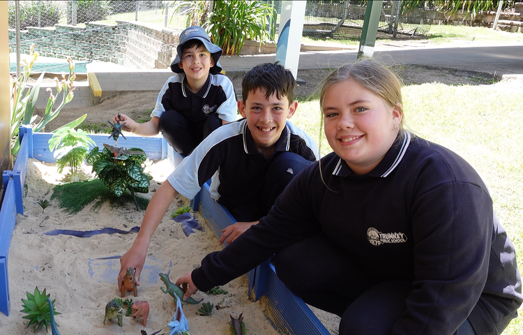 3 Trunkey Public School students playing in the dinosaur environment and smiling at the camera