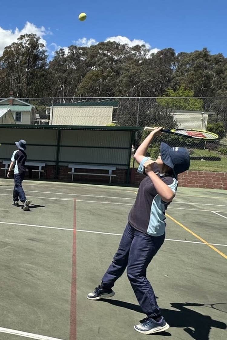 A student hitting a ball with a tennis racket on the multi-purpose sports court.