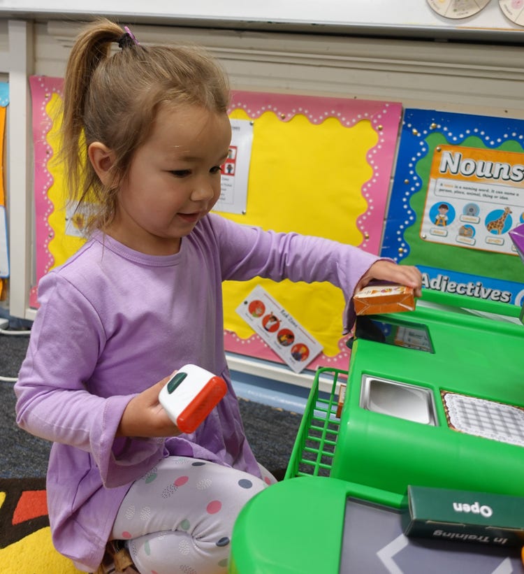 A child holding a pretend food item and scanner at a play shop.