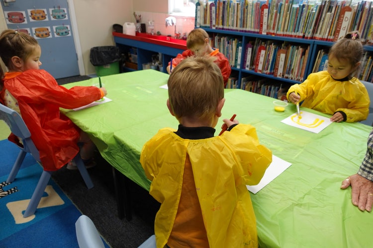 4 children sitting at a table wearing paint shirts and painting pictures