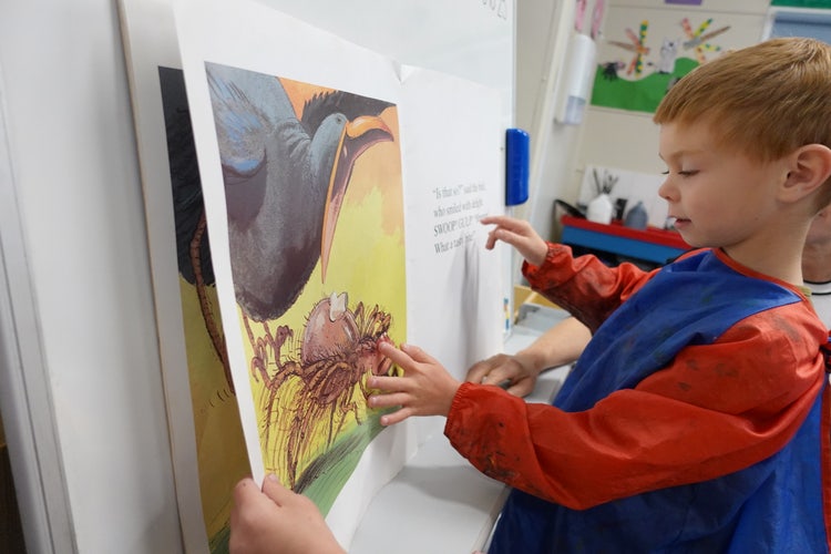 A child standing and looking at a book, with finger following the words on the page.