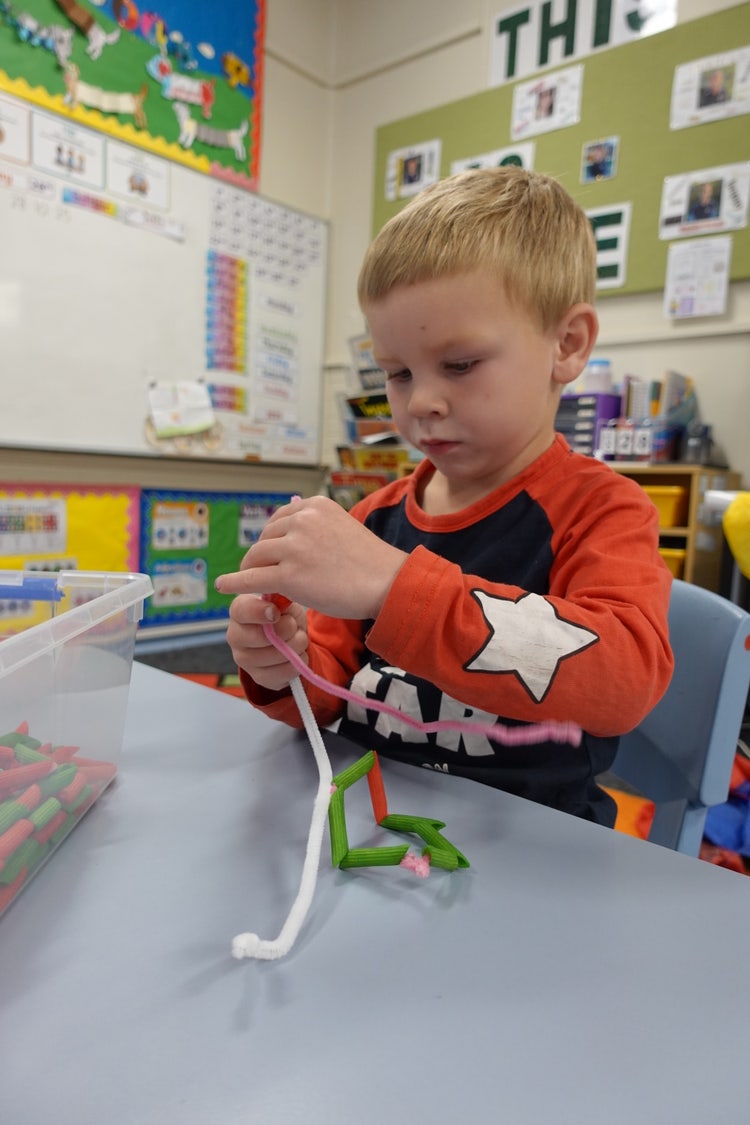 A child sitting at a table threading red and green pasta onto pipe cleaners