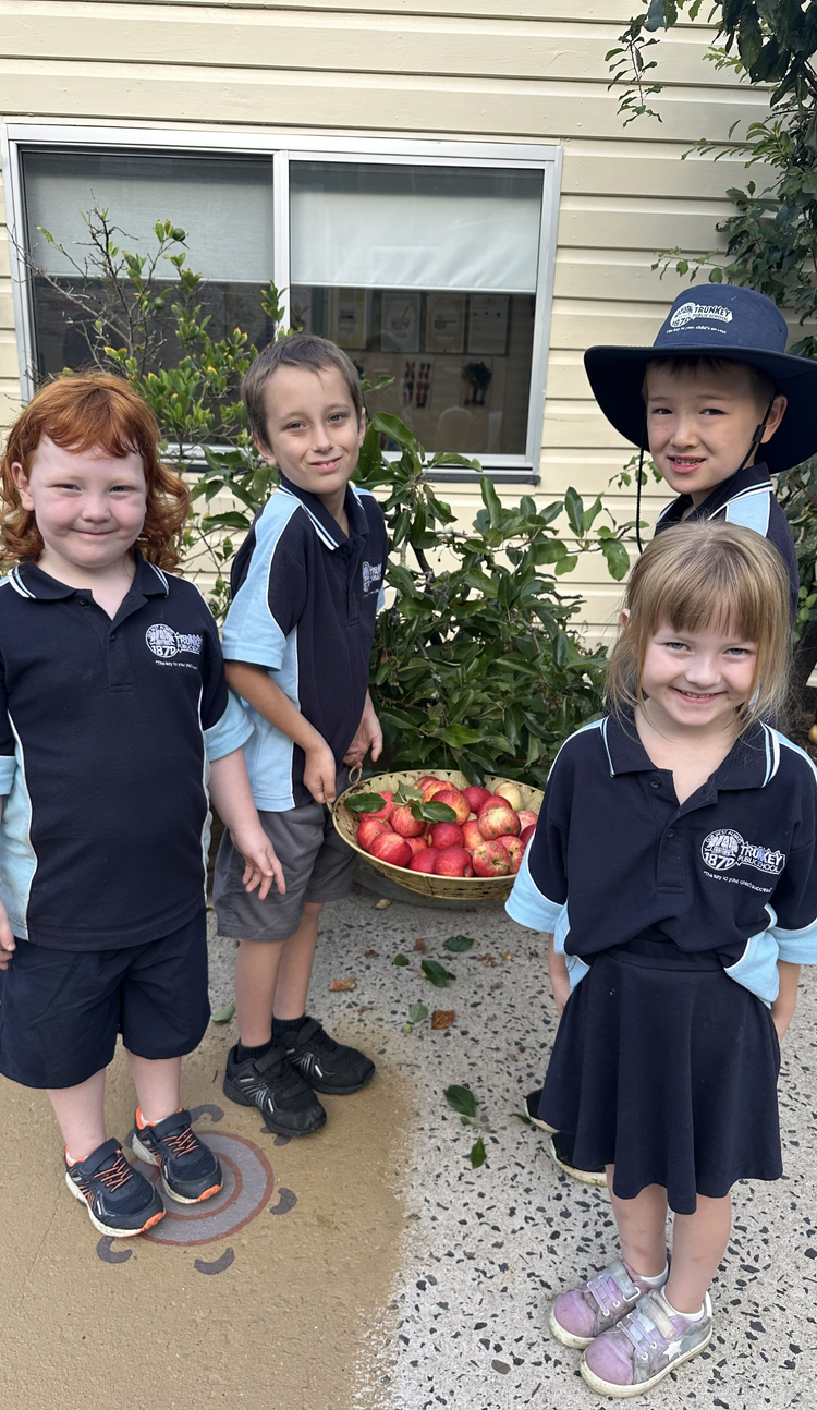 Trunkey Public School students with a basket of fresh apples standing beside our fruit trees