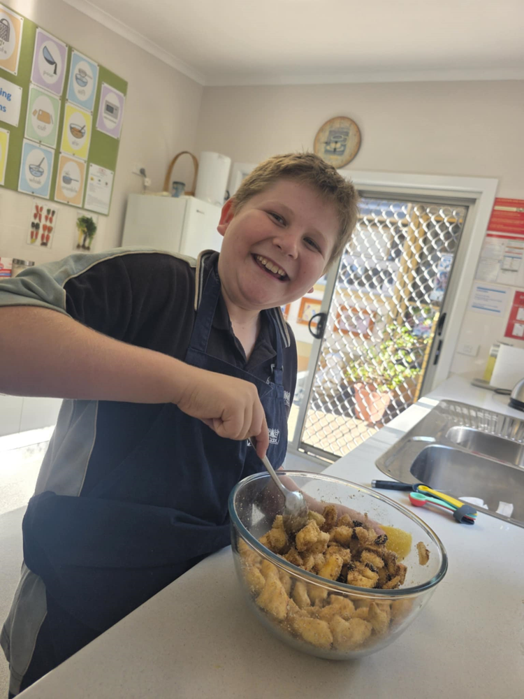 A student smiling at the camera while stirring a bowl of ingredients
