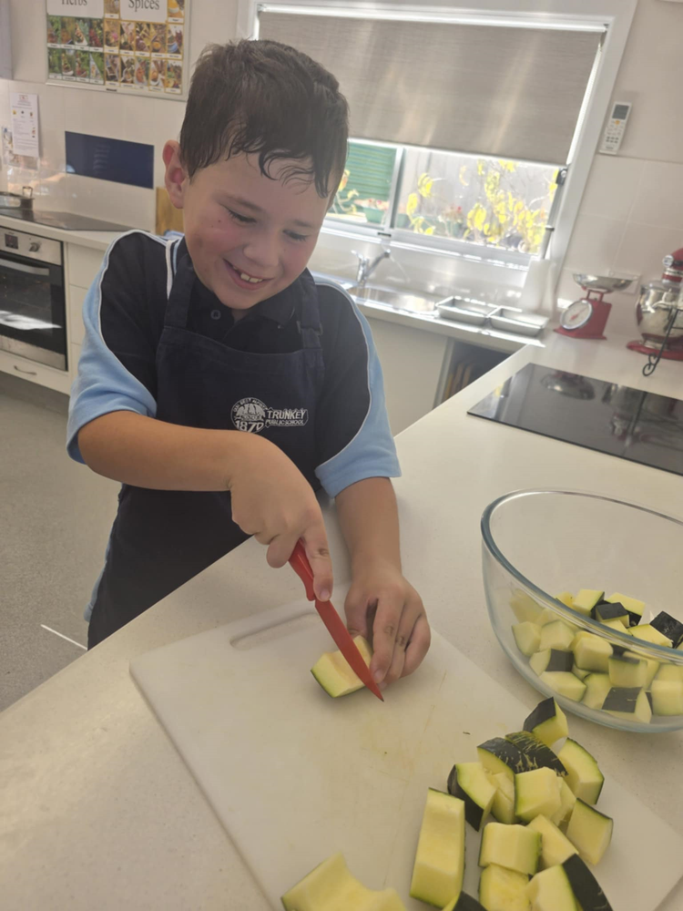 A student using a small knife on a chopping board to cut zucchini