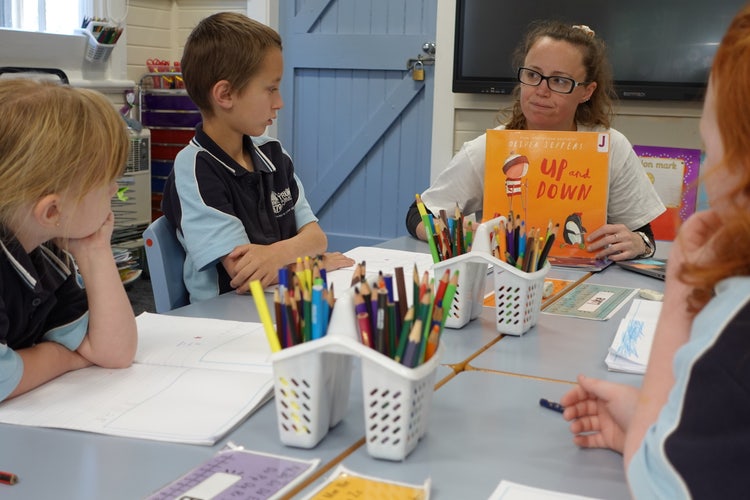Infants students at their desks with Miss Bermingham holding the book