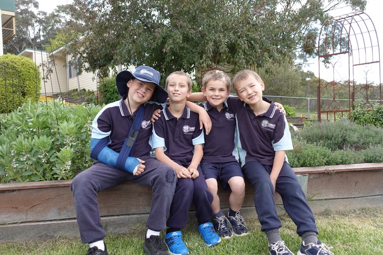 Four Trunkey Public School students sitting on the edge of a vegetable garden bed, smiling with their arms around each other.