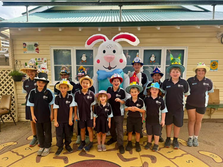 14 students wearing their Easter hat parade hats and standing with the Easter Bunny