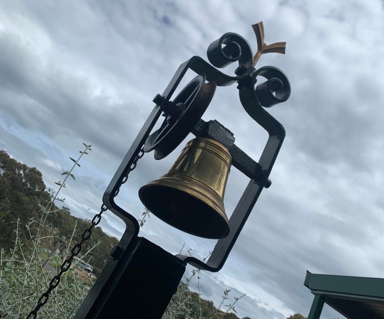 Old school bell, still functional, against cloudy sky.