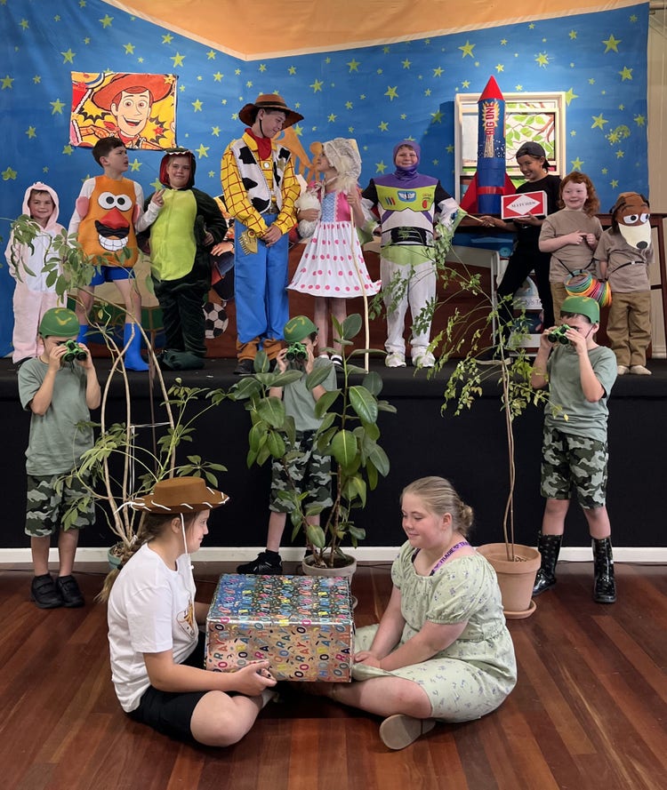 14 students dressed up as the characters from Toy Story. Students are posed on the stage with props and a backdrop in a cast photo.