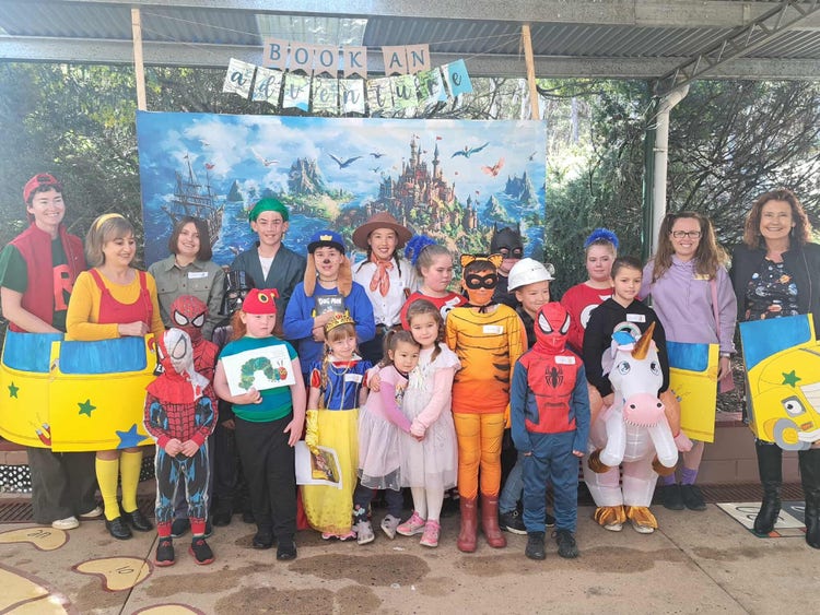 Staff and students dressed up in costumes for book week, standing in front of a castle back drop with banner saying