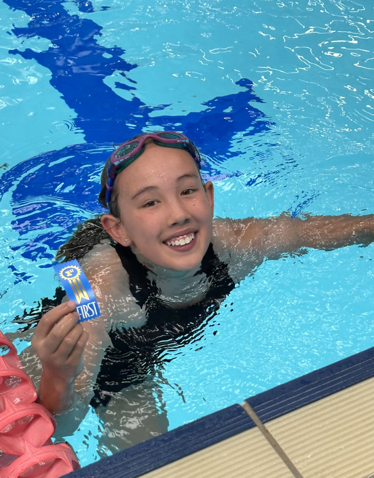 Trunkey Public School student, Erica Langworthy, in a swimming pool after finishing a race, holding a blue ribbon.ue