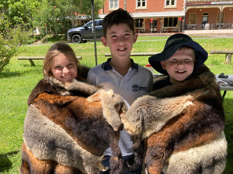 3 Trunkey Public School students wrapped in a possum skin coat
